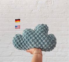 a hand holding up a crocheted cloud with a german flag in the background