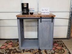 a small table with a sign on it next to a coffee pot and cup holder