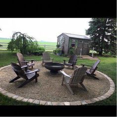 a fire pit surrounded by lawn chairs in the middle of a yard with a shed in the background