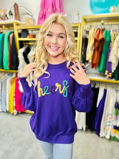 a blonde woman standing in front of a rack of clothes and smiling at the camera