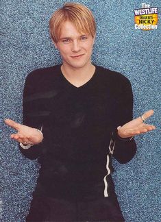 a young man posing for a photo in front of a blue wall with his hands out