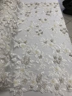 a white table cloth with flowers and leaves on the top, in front of a tiled floor