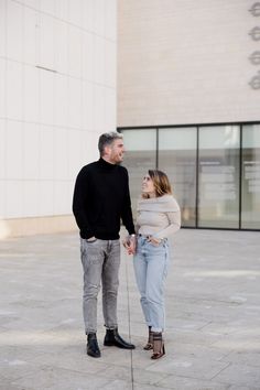 a man and woman standing next to each other in front of a building holding hands