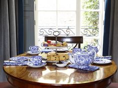 a wooden table topped with blue and white plates filled with food next to a window