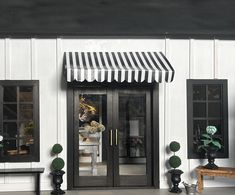 a black and white striped awning on the front door of a house with potted plants