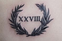 a tattoo with roman numerals and an olive wreath on the back of a woman's shoulder