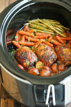 a slow cooker filled with chicken, carrots and asparagus on a wooden table