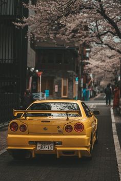 a yellow car is parked on the side of the road in front of cherry blossom trees