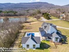 an aerial view of a home in the mountains with a lake and wooded area behind it