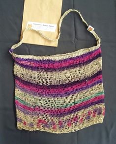 a crocheted bag sitting on top of a bed next to a paper bag