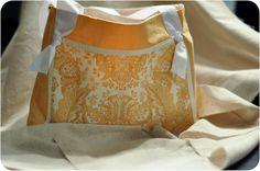 an orange and white purse sitting on top of a cloth covered tablecloth with ribbon tied around it