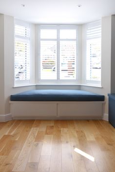 a window seat in the corner of a room with wooden floors and white shutters