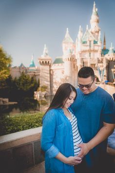 a man and woman standing next to each other in front of a castle at disneyland