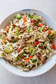 a white bowl filled with broccoli, carrots and sprouts covered in shredded cheese