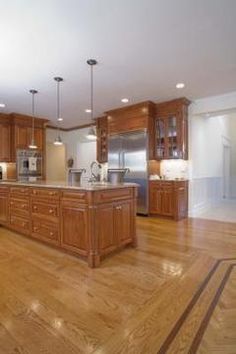 a large kitchen with wooden cabinets and stainless steel appliances in the center, along with hardwood flooring