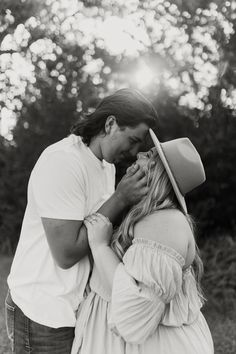 black and white photograph of a man kissing a woman's forehead in front of trees