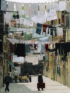 people walking down an alley way with laundry hanging from the clothes line above them,