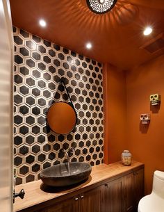 an orange bathroom with black and white tiles on the wall, round mirror above the sink