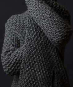 a person wearing a gray knitted sweater and holding their hands up to their face