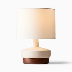 a white table lamp with a wooden base and a cream shade on the top, against a white background