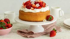 there is a cake with strawberries on the top and two cups next to it