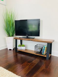 a flat screen tv sitting on top of a wooden shelf next to a potted plant