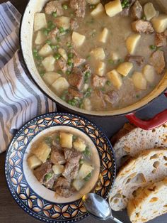 a bowl of soup with meat and potatoes next to some slices of bread on a table