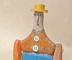 a small wooden toy with a yellow hat on it's head and legs, sitting in front of a white wall