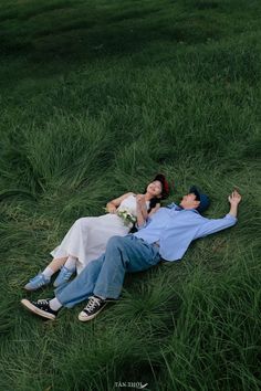 a man and woman laying on the ground in tall grass with their arms around each other