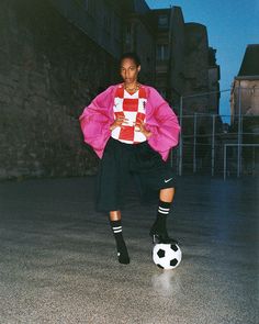 a woman standing on top of a soccer ball wearing a pink jacket and black pants