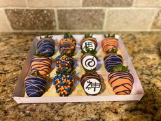 chocolate covered strawberries with orange and blue icing in a box on a counter