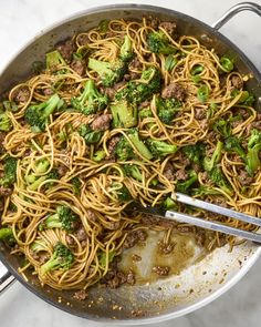 a wok filled with noodles and broccoli on top of a white counter