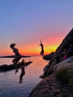 three people jumping off rocks into the water at sunset or dawn with their arms in the air