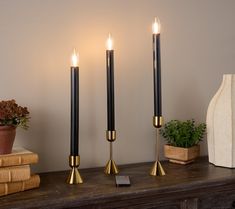 three candles are sitting on top of a table next to some books and a plant