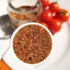 a white plate topped with a bowl filled with brown stuff next to tomatoes and other vegetables