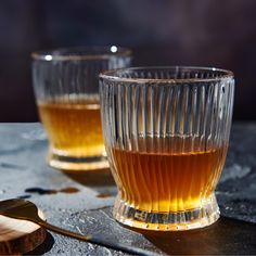 two glasses filled with liquid sitting on top of a table next to a wooden spoon