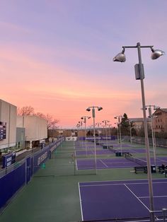 an outdoor tennis court with several lights on each side and purple skies in the background