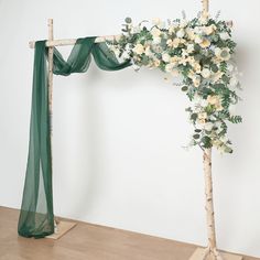 an arch with flowers and greenery on it is shown in front of a white wall