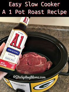 a hand holding a bottle of sauce next to a slow cooker with meat in it