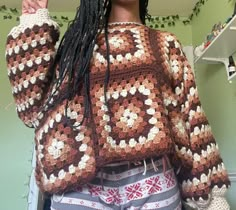 a woman with dreadlocks is wearing a crocheted sweater and holding her hand up in the air