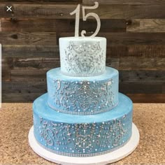 a three tiered cake with blue frosting and white icing on top is displayed against a wooden wall