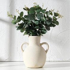 a white vase with some green plants in it