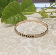 MAKE SURE OF THE SIZE BEFORE ORDERING. 5mm gold filled Hawaiian bangle, 1.70mm thickness. Personalize it with a name or a message engraved and enameled in black. The pattern of plumerias and Victorian scrolls are rolled on a 5mm barrel gold filled wire. All the characters are engraved , not stamped, resulting in straight and aligned name. A black enamel is used to fill in the characters engraved. The maximum number of letters is 15. How Gold filled is made. Gold filled or gold overlay is made by Etched Yellow Gold Bangle For Anniversary, Black Engraved Name Bracelet For Anniversary, Gold Hand Stamped Jewelry For Promise, Etched 14k Gold Bangle As A Gift, 14k Gold Etched Bangle Perfect For Gifting, Gift 14k Gold Etched Bangle, 14k Gold Etched Bangle Perfect As A Gift, Gold Bracelets With Engraving Option For Promise, Gold Engraved Bangle For Anniversary