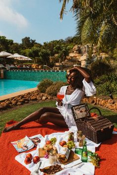 a woman sitting on the ground with food and drinks in front of an outdoor pool