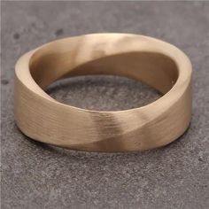 a close up of a gold ring on a gray surface with the middle part of it slightly bent