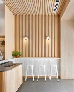 three white stools in front of a counter with potted plants on it and wooden slatted walls