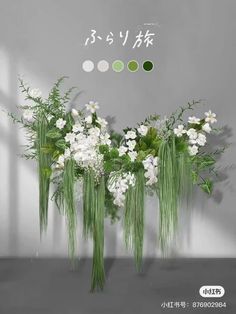 an arrangement of white flowers and greenery in front of a gray wall with chinese writing