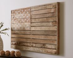 a wooden wall hanging on the side of a white wall with vase and pine cones