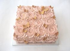 a square cake with pink frosting and gold leaves on the top, sitting on a white surface