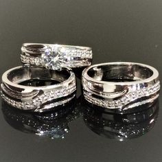 three wedding rings are shown on a black surface with reflective reflection in the middle and one is white gold